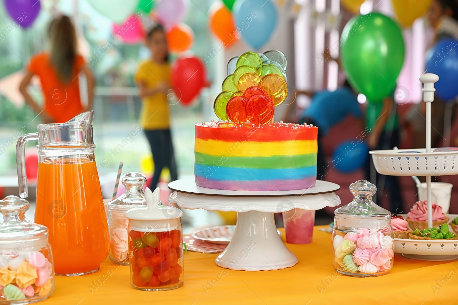 Photo of Bright birthday cake and other treats on table in decorated room