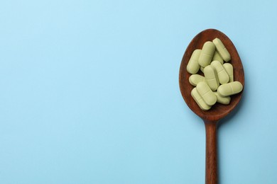 Photo of Vitamin pills in wooden spoon on light blue background, top view. Space for text