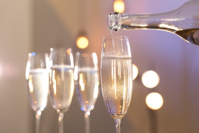 Photo of Champagne pouring from bottle into glass on blurred background, closeup. Space for text