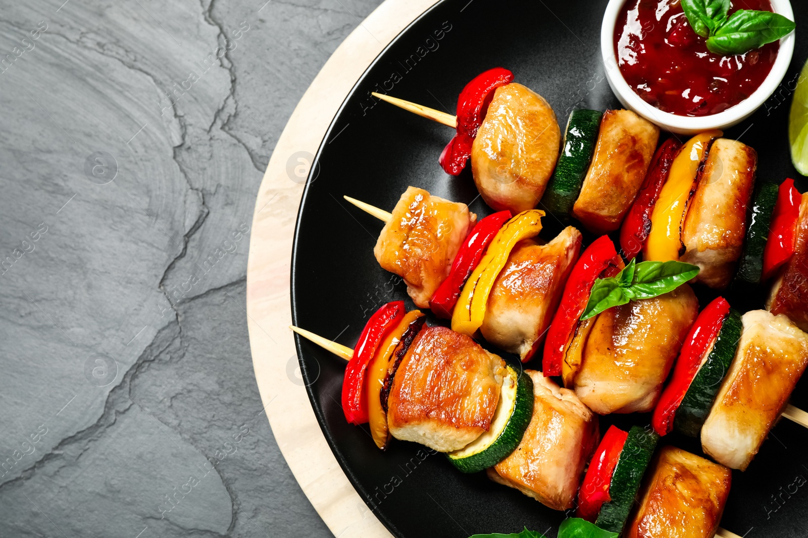 Photo of Delicious chicken shish kebabs with vegetables and sauce on grey table, top view