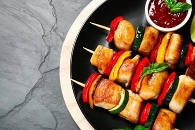 Delicious chicken shish kebabs with vegetables and sauce on grey table, top view