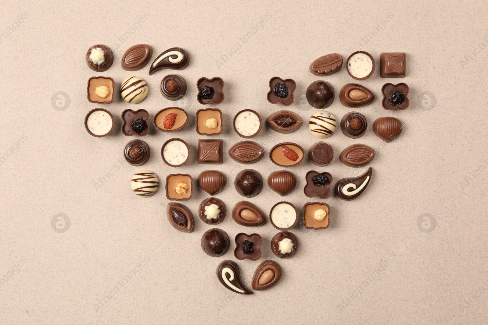 Photo of Heart made with delicious chocolate candies on beige background, top view