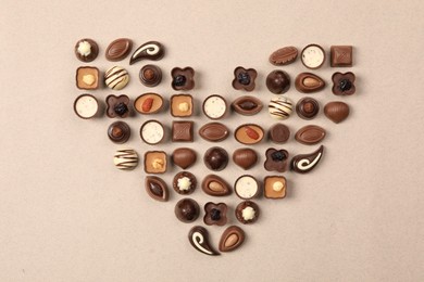 Heart made with delicious chocolate candies on beige background, top view