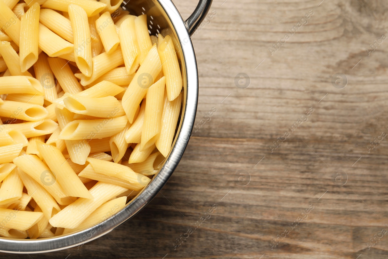 Photo of Delicious penne pasta in colander on wooden table, top view. Space for text