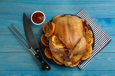 Photo of Delicious chicken with oranges and pomegranate on light blue wooden table, flat lay