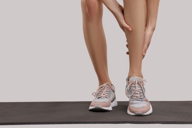 Woman suffering from leg pain on exercise mat against grey background, closeup. Space for text