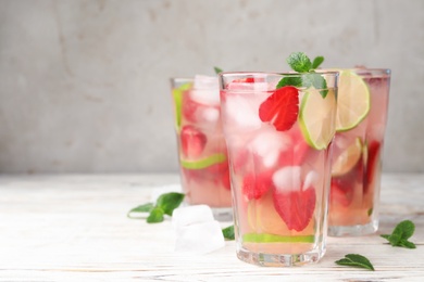 Glasses of refreshing drink with strawberry, lime and mint on light wooden table against grey background, space for text