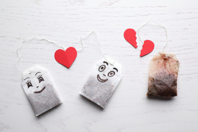 Photo of Tea bags with drawn faces on white wooden background, flat lay. Concept of jealousy