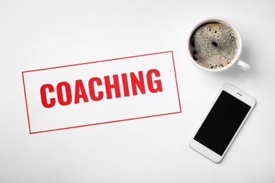 Photo of Word COACHING, mobile phone and cup of coffee on white background. Business trainer concept