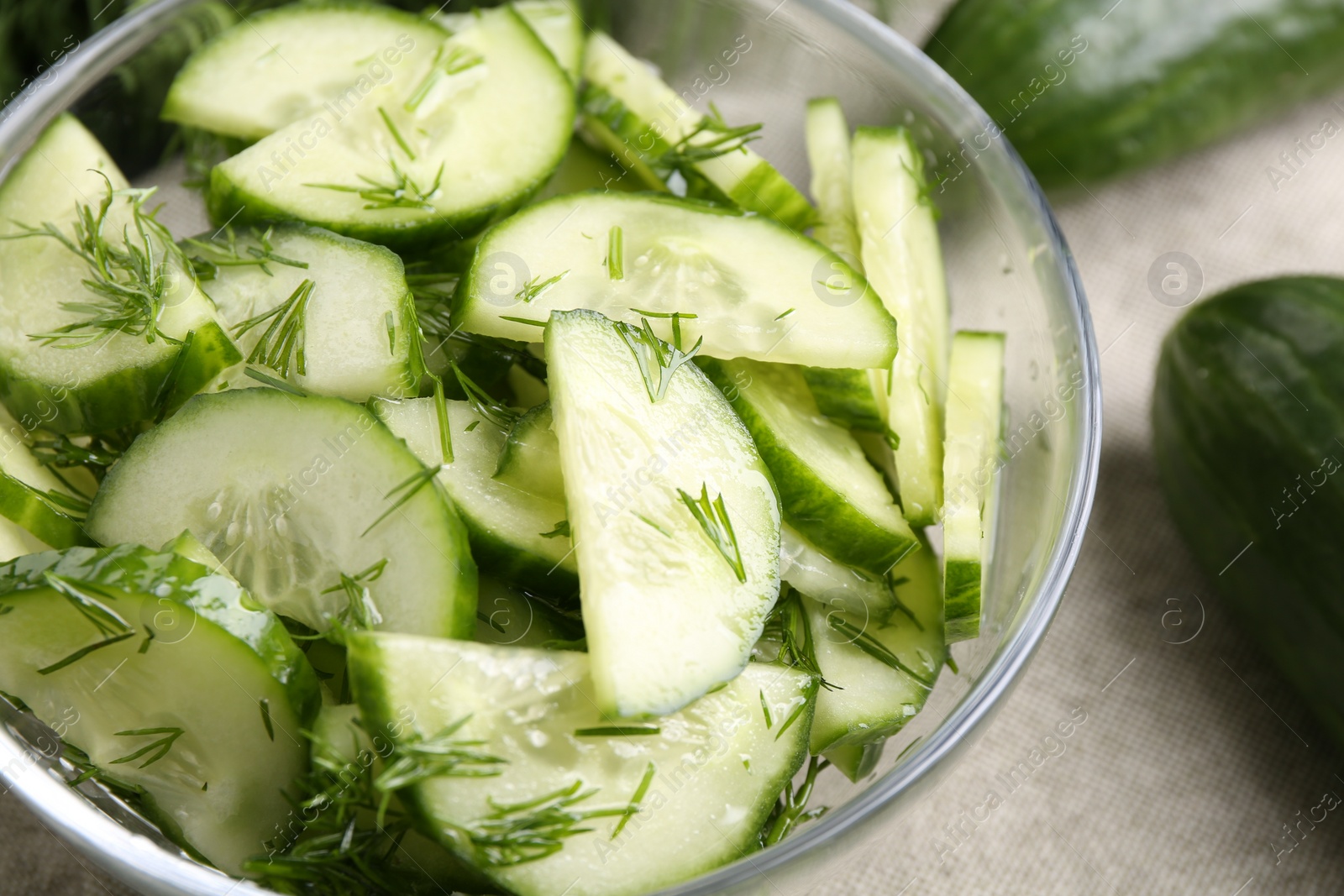 Photo of Cut cucumber with dill in glass bowl and fresh vegetables on table, closeup