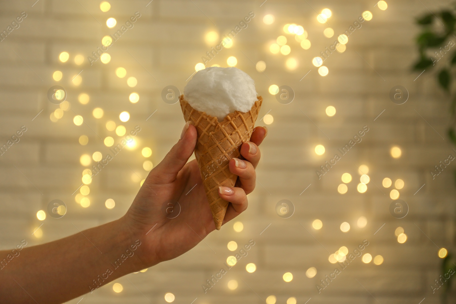 Photo of Woman holding waffle cone with cotton candy against blurred lights, closeup