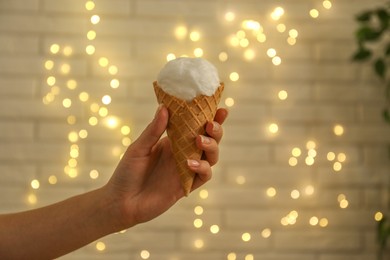 Photo of Woman holding waffle cone with cotton candy against blurred lights, closeup