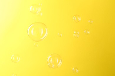 Photo of Beautiful transparent soap bubbles on yellow background