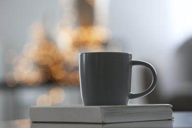 Book and cup on table against blurred background with bokeh effect, closeup