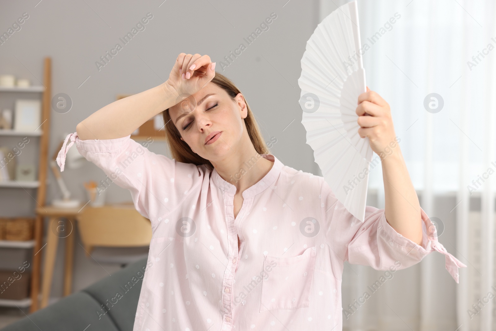 Photo of Woman waving white hand fan to cool herself at home