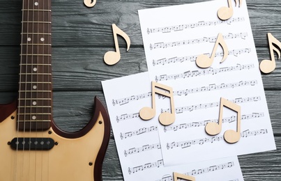 Guitar and sheets with music notes on wooden background, top view
