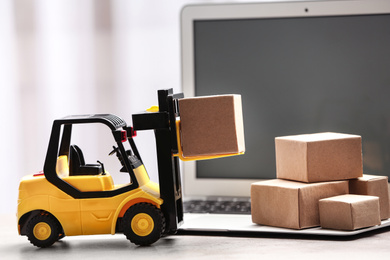 Photo of Toy forklift with box near laptop on table. Logistics and wholesale concept