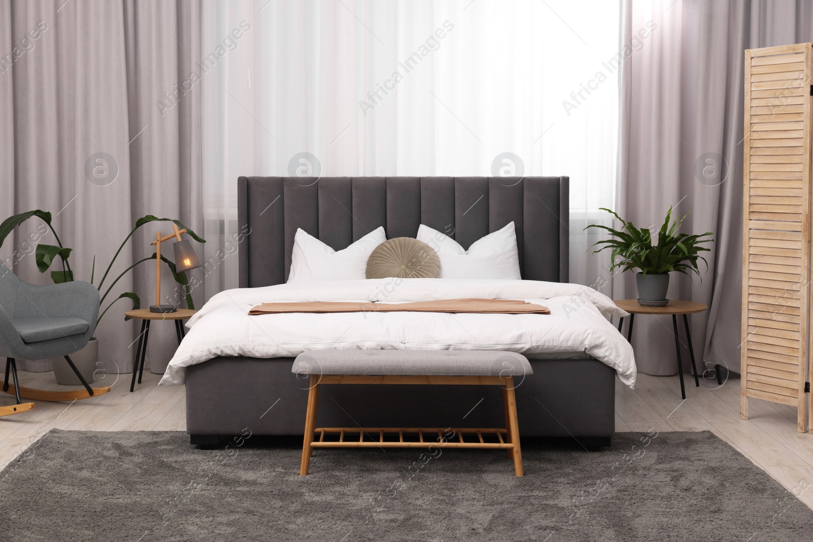 Photo of Stylish bedroom interior with large bed, ottoman, lamp and houseplants