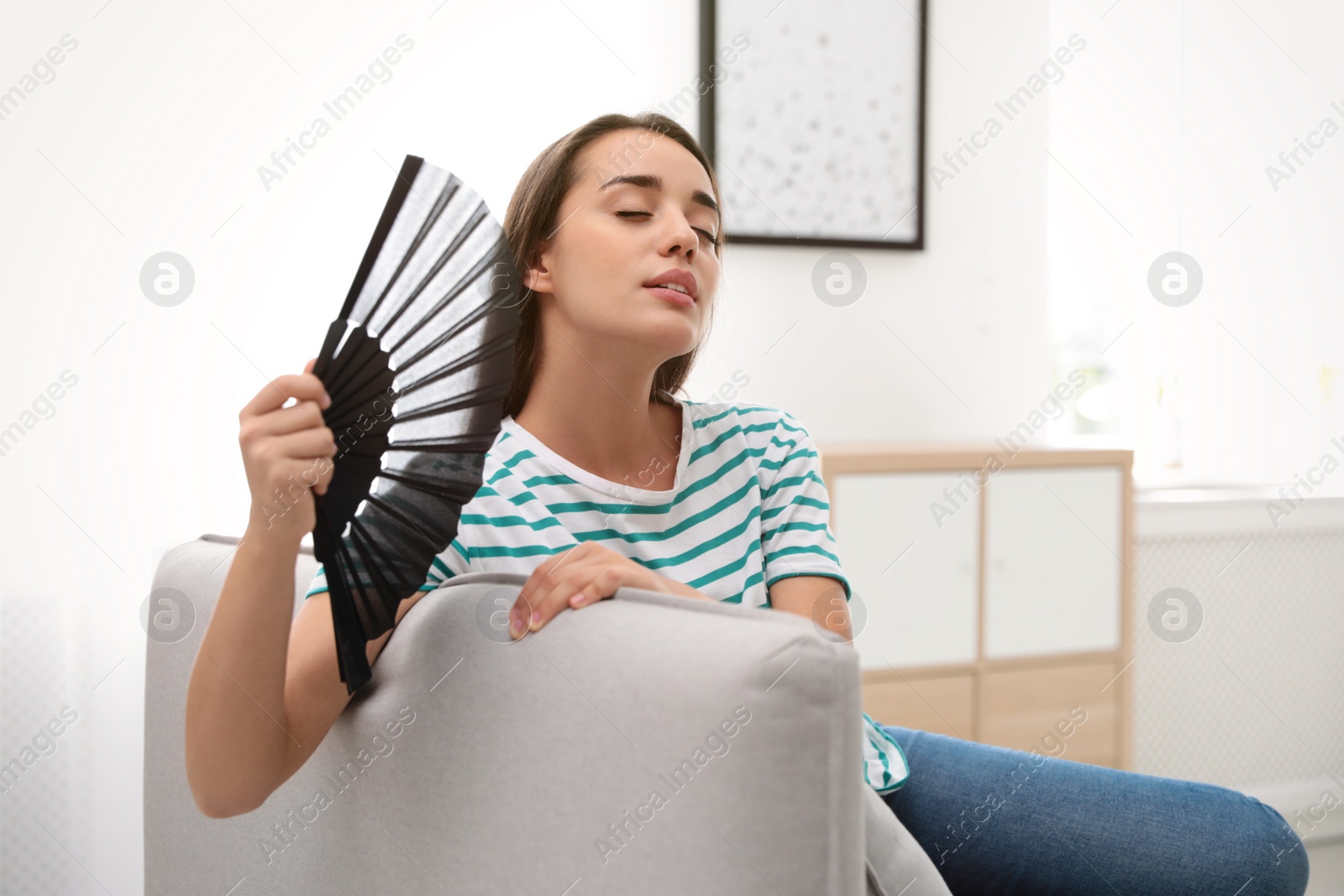 Photo of Woman enjoying air flow from hand fan at home. Summer heat