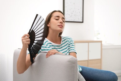 Photo of Woman enjoying air flow from hand fan at home. Summer heat