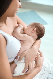 Young woman breastfeeding her baby on blurred background, closeup