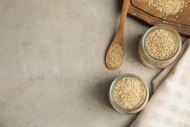 Photo of Jars and spoon with white quinoa on light grey table, flat lay. Space for text