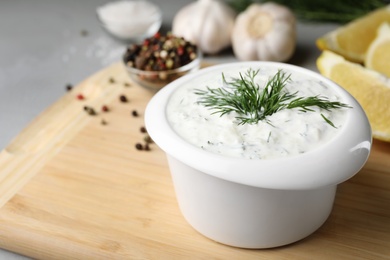 Photo of Bowl with cucumber sauce on wooden board, space for text