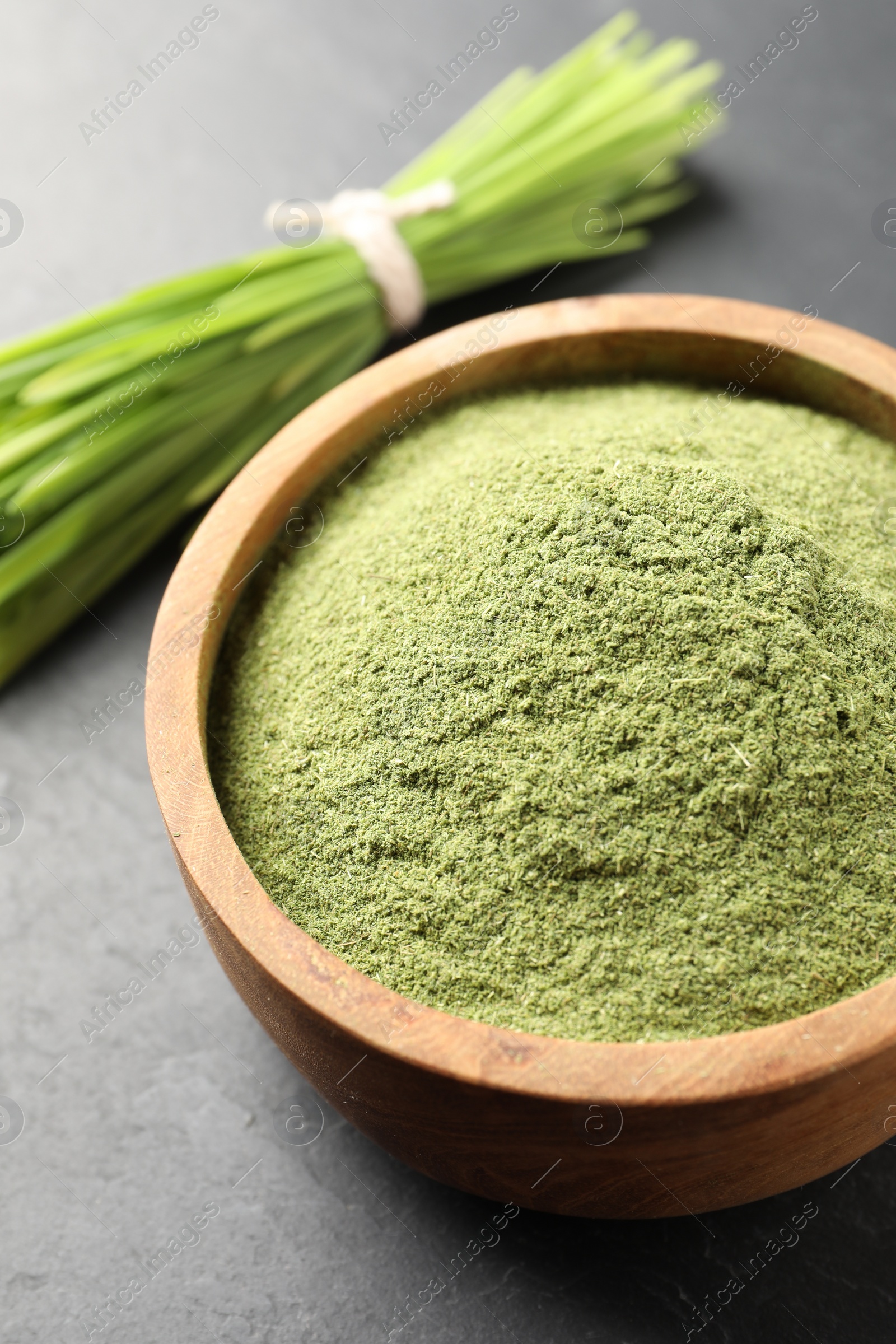 Photo of Wheat grass powder in bowl on grey table, closeup
