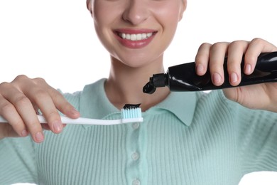Photo of Woman applying charcoal toothpaste onto brush on white background, closeup