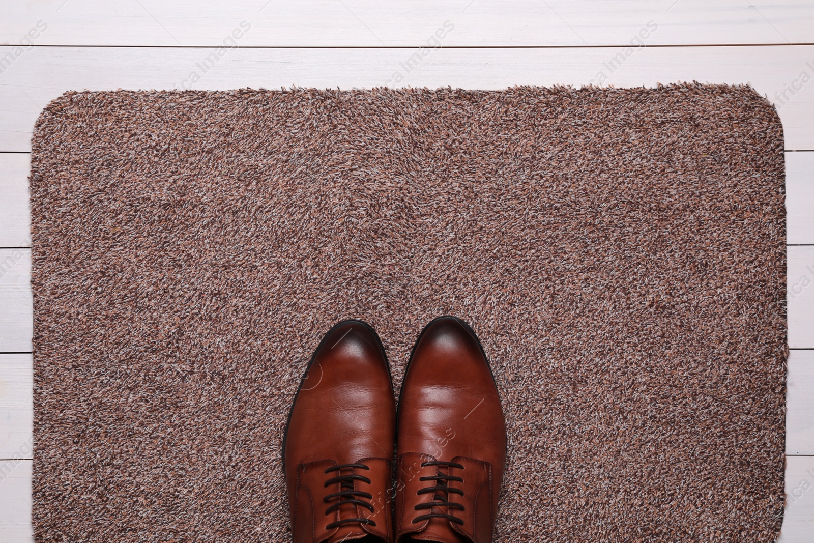 Photo of New clean door mat with shoes on white wooden floor, top view