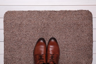 Photo of New clean door mat with shoes on white wooden floor, top view