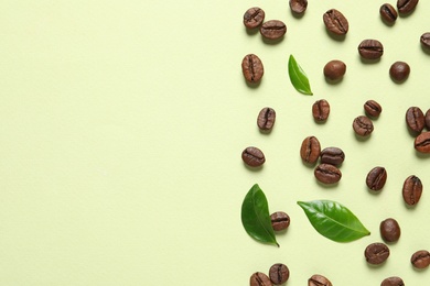 Photo of Fresh green coffee leaves and beans on light green background, flat lay. Space for text