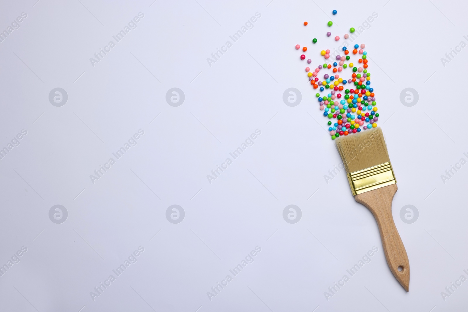 Photo of Brush painting with colorful sprinkles on light background, top view. Space for text. Creative concept