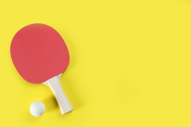Photo of Ping pong racket and ball on yellow background, flat lay. Space for text