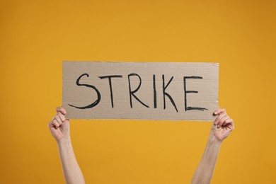 Photo of Woman holding cardboard banner with word Strike on orange background, closeup