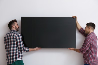 Photo of Men installing modern flat screen TV on wall indoors
