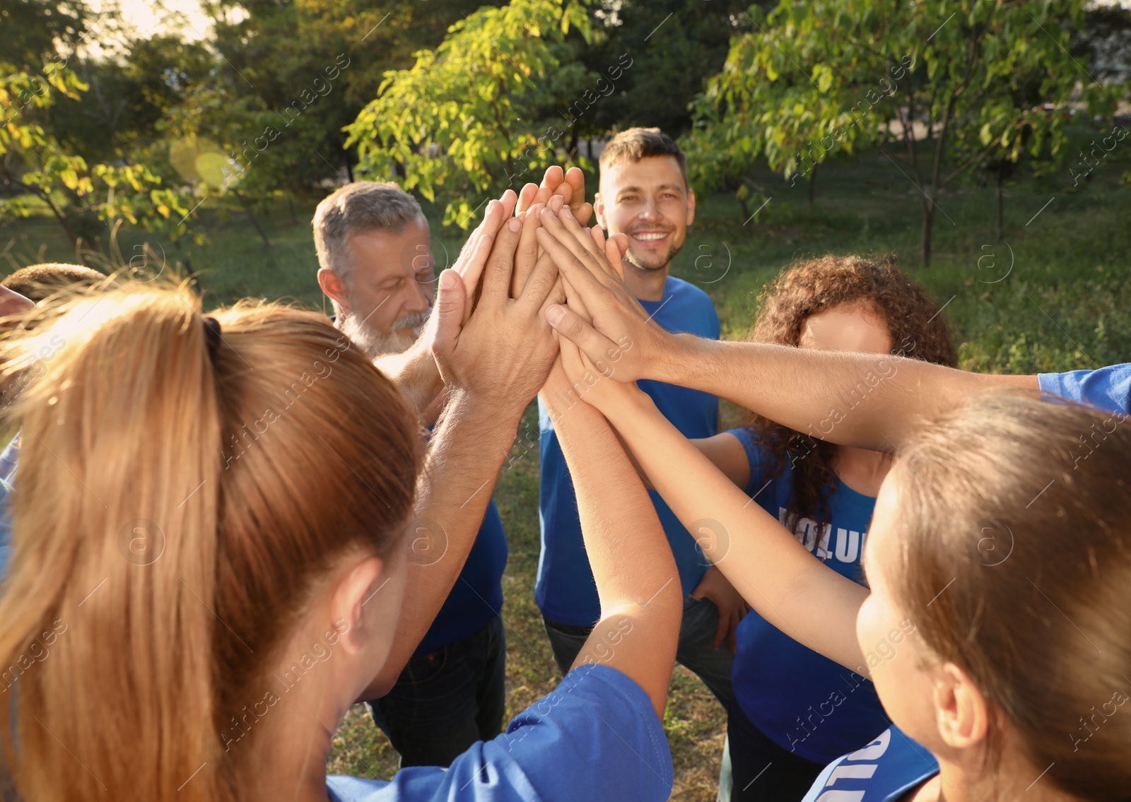 Photo of Group of volunteers joining hands together outdoors on sunny day