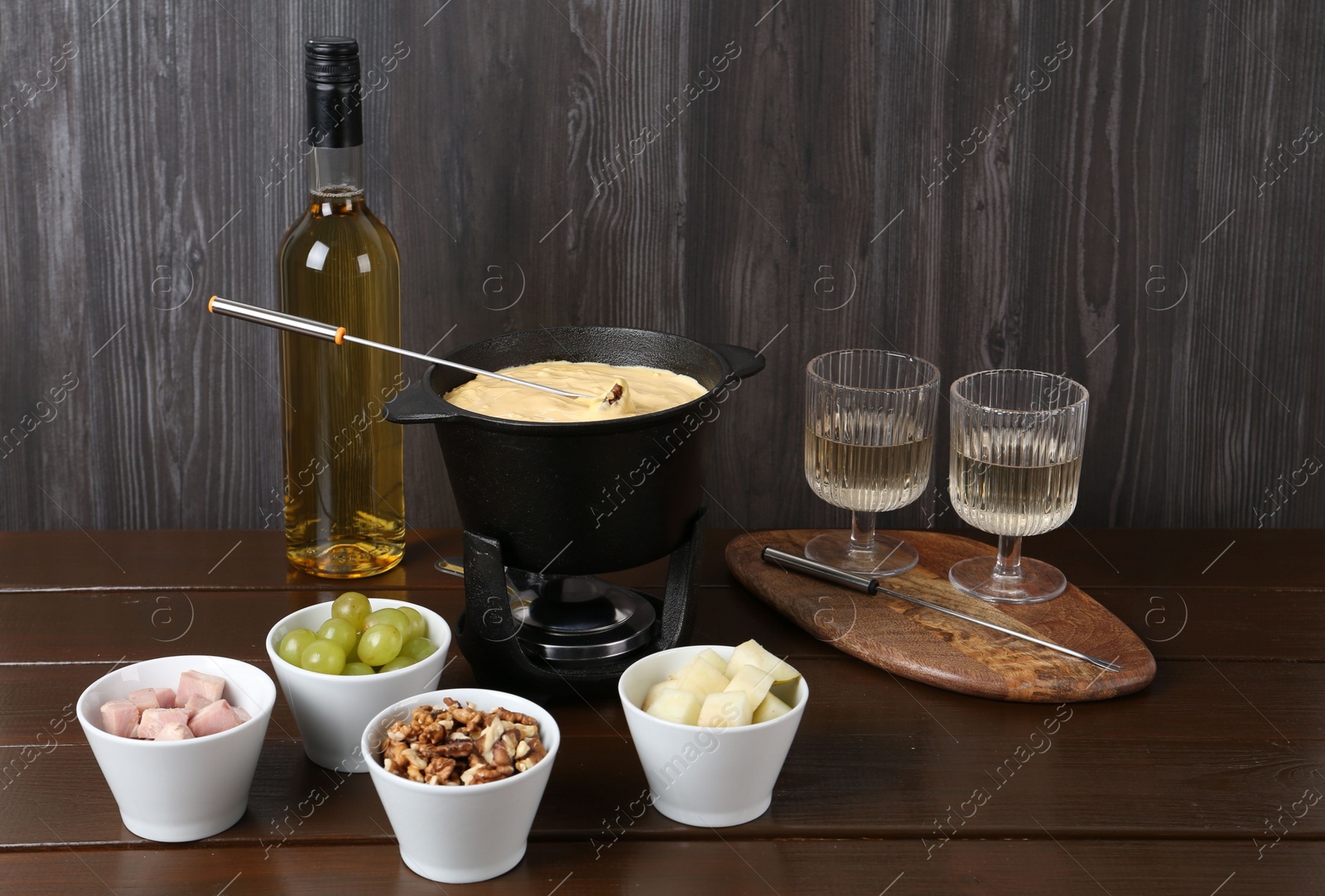 Photo of Fondue pot with tasty melted cheese, forks, wine and different snacks on wooden table