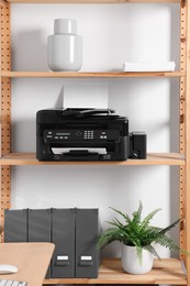 Modern printer with paper on wooden shelf in home office