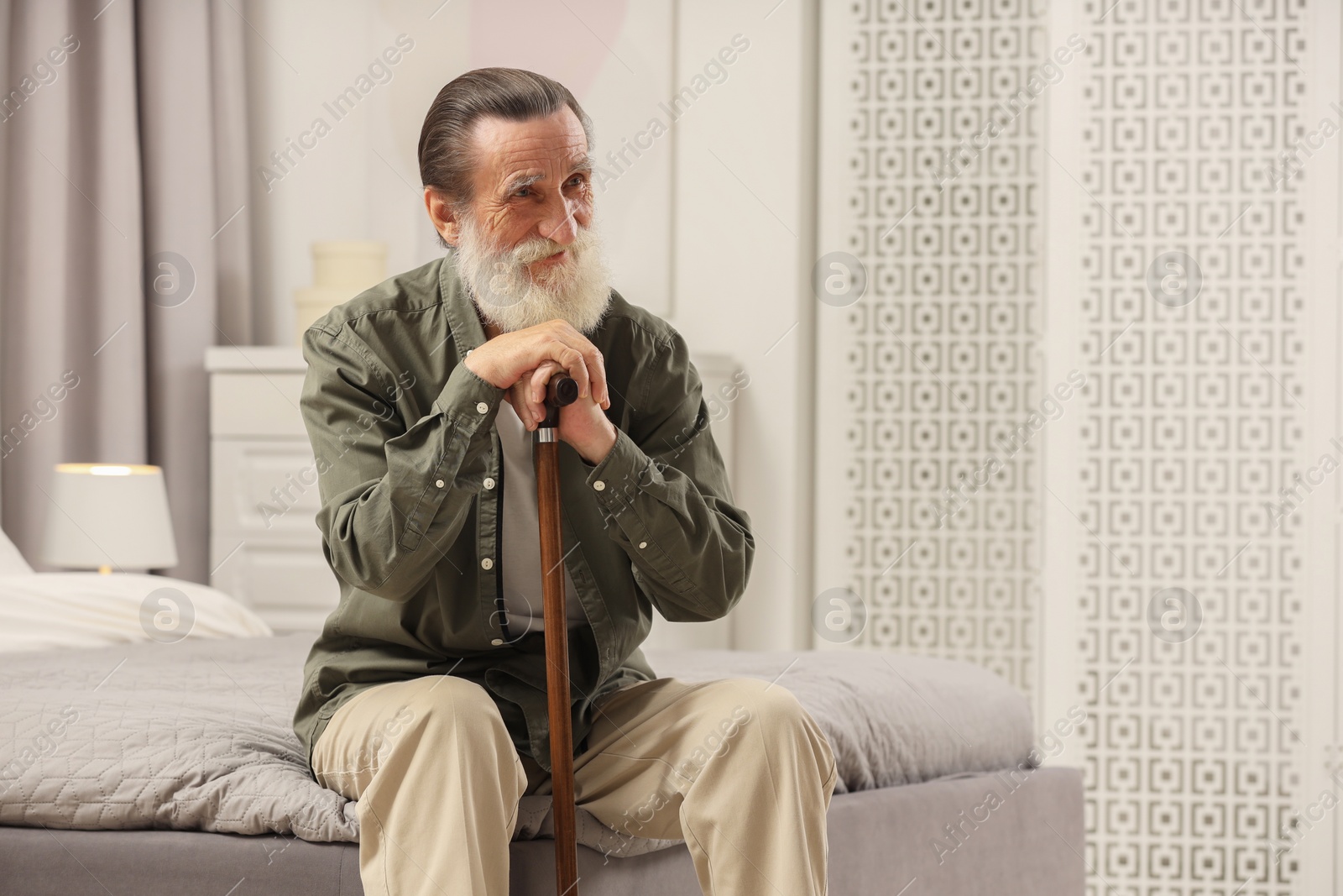 Photo of Senior man with walking cane on bed at home