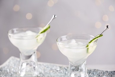 Glasses of martini with cucumber on tray against light background, closeup. Space for text