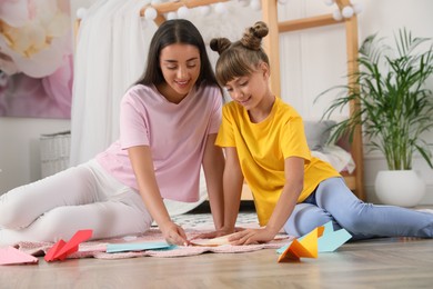 Photo of Happy mother and daughter making paper planes on floor in room