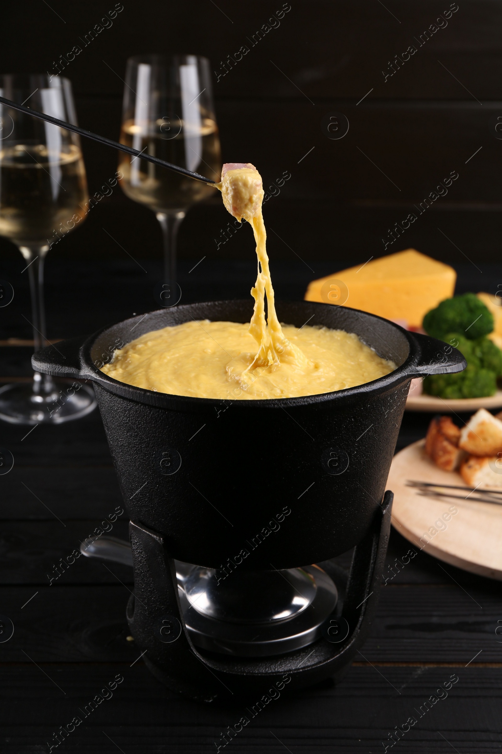 Photo of Dipping piece of ham into fondue pot with melted cheese on table