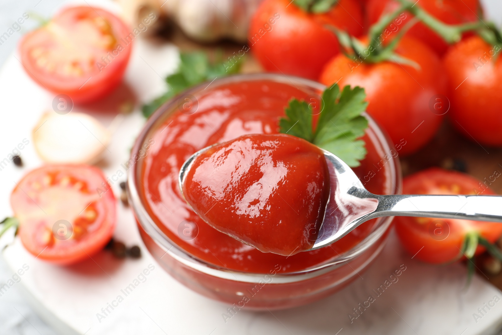 Photo of Taking delicious tomato ketchup with spoon from bowl at light table, closeup