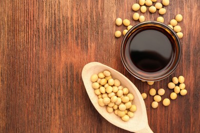 Photo of Soy sauce in bowl and soybeans on wooden table, flat lay. Space for text