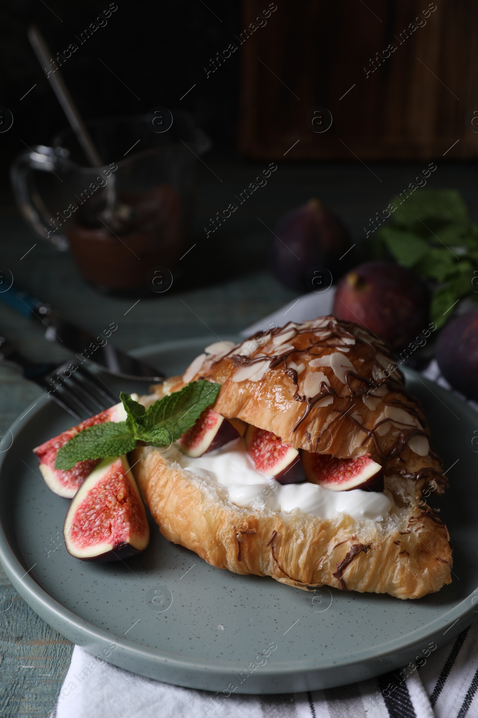 Photo of Delicious croissant with figs and cream served on light blue wooden table