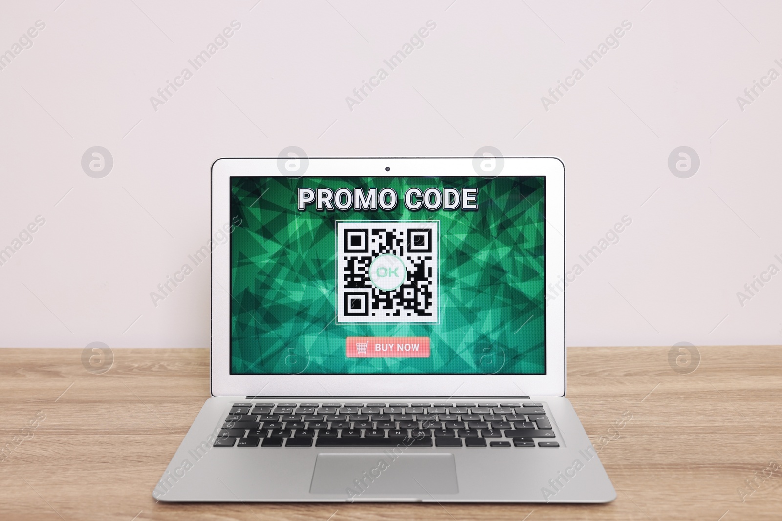 Photo of Laptop with activated promo code on wooden table near white wall