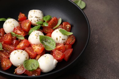 Tasty salad Caprese with tomatoes, mozzarella balls and basil on brown table, closeup