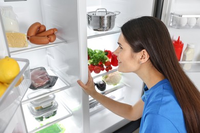 Young smiling woman looking into modern refrigerator