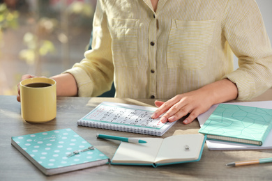 Woman with calendar and cup of drink at wooden table, closeup